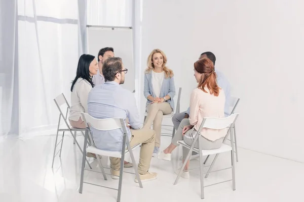Personas multiétnicas de mediana edad sentadas en sillas y hablando durante la terapia de grupo - foto de stock
