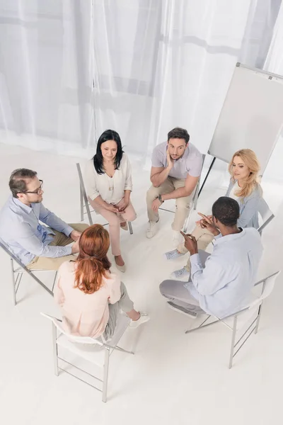 Blick von oben auf multiethnische Menschen mittleren Alters, die auf Stühlen sitzen und sich während der Gruppentherapie unterhalten — Stockfoto