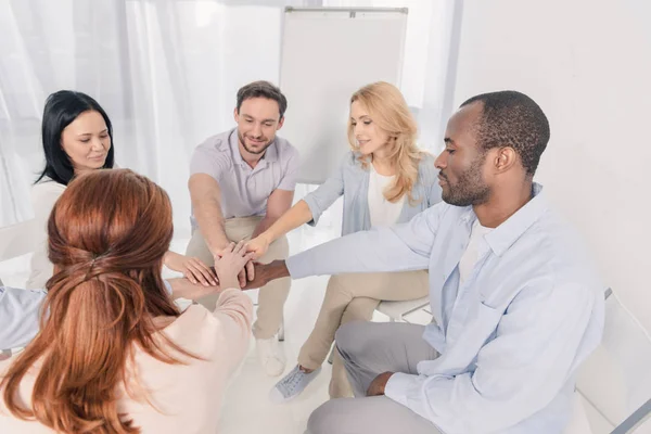 Sonrientes personas multiétnicas de mediana edad que apilan las manos durante la terapia de grupo - foto de stock