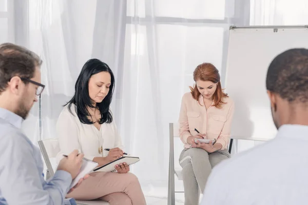 Personas multiétnicas de mediana edad que toman notas durante la terapia de grupo - foto de stock