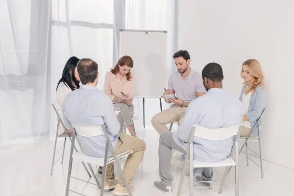 Multiethnic middle aged people taking notes in notebooks during group therapy — Stock Photo
