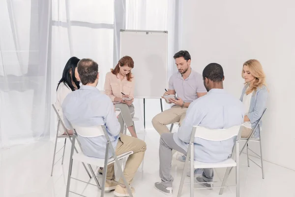 Multiethnische Menschen mittleren Alters notieren während der Gruppentherapie Notizen in Notizbüchern — Stockfoto