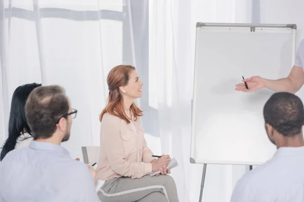 Recortado de psicoterapeuta apuntando a pizarras blancas y personas multiétnicas sentadas en sillas durante la terapia de grupo - foto de stock