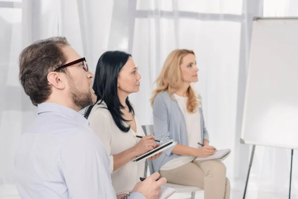 Middle aged people with notebooks looking away while sitting at anonymous group therapy — Stock Photo