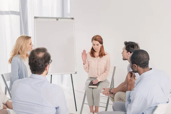 Woman with closed eyes holding hand on Holy Bible while sitting with multiethnic people during group therapy — Stock Photo