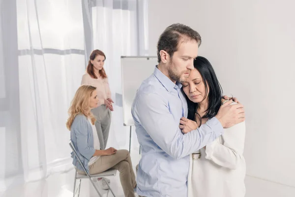 Зрілий чоловік обіймає пригнічену азіатську жінку під час групової терапії — стокове фото