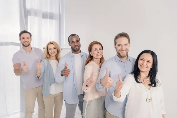 Pessoas multiétnicas de meia-idade sorrindo para a câmera e mostrando os polegares para cima durante a terapia de grupo — Fotografia de Stock