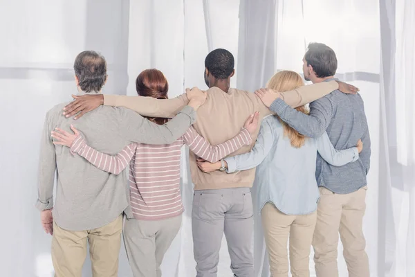 Vue arrière de personnes multiethniques debout et embrassant pendant la thérapie de groupe — Photo de stock