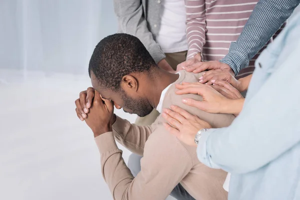 Abgeschnittene Aufnahme von Menschen, die einen depressiven afrikanisch-amerikanischen Mann während einer Gruppentherapie unterstützen — Stockfoto