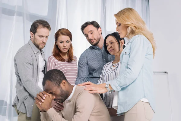 Groupe multiethnique de personnes soutenant l'homme afro-américain bouleversé pendant la thérapie — Photo de stock