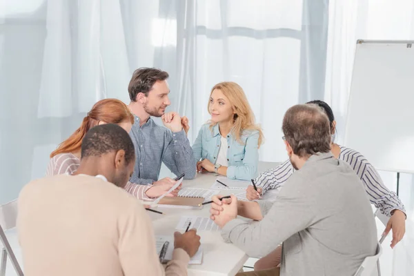 Multiethnische Gruppe von Menschen, die zusammenarbeiten und Notizen machen, während sie sich unterhalten — Stockfoto