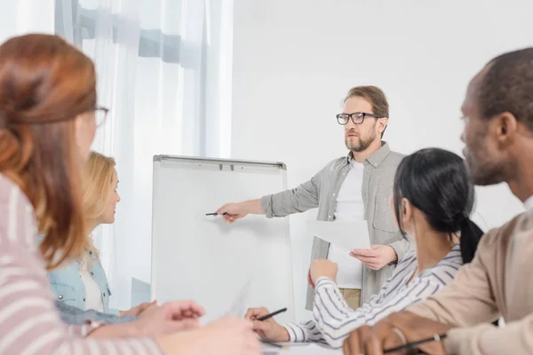 Male psychoanalyst pointing at whiteboard white people gathered around table at anonymous group therapy — Stock Photo