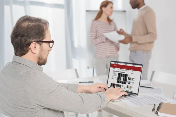 Middle aged man in in eyeglasses using laptop with bbc news website on screen in office — Stock Photo