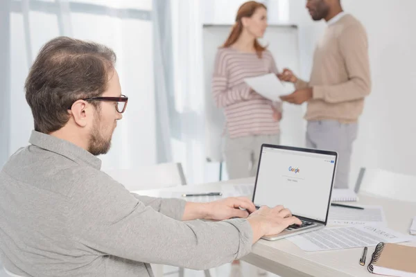 Middle aged man in in eyeglasses using laptop with google website on screen in office — Stock Photo