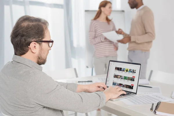 Hombre de mediana edad en gafas con portátil con sitio web de youtube en la pantalla en la oficina - foto de stock