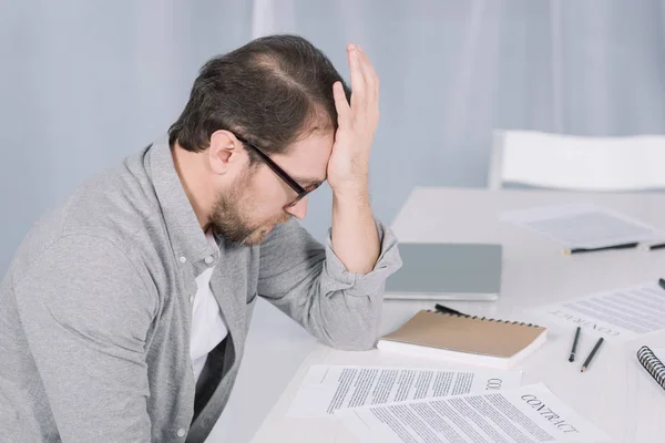 Depressiver, überarbeiteter Geschäftsmann sitzt mit Papieren im Büro am Tisch — Stockfoto