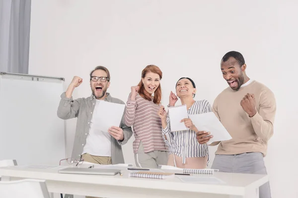 Glückliche multiethnische Menschen mittleren Alters, die Papiere halten und triumphieren — Stockfoto