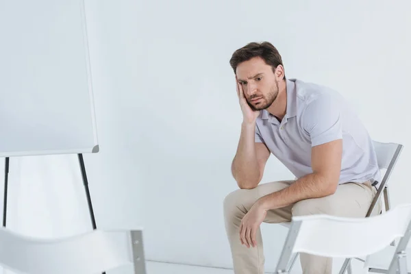 Hombre deprimido sentado y mirando hacia otro lado en una habitación vacía - foto de stock