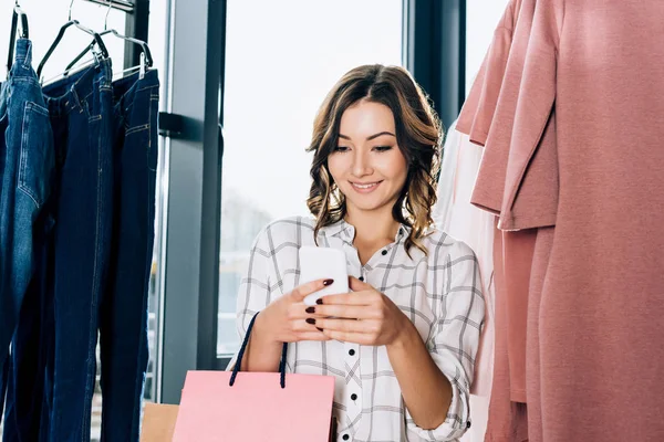 Lächelnde junge Frau beim Einkaufen mit Smartphone — Stockfoto