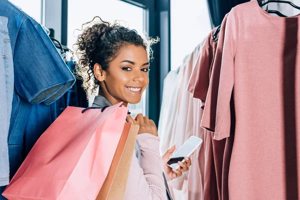 Beautiful young woman with smartphone and shopping bags in clothing store — Stock Photo