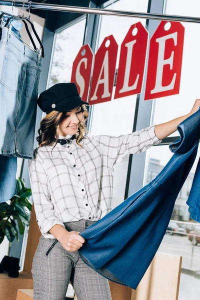 Stylish young woman looking at blue denim dress at clothing store — Stock Photo