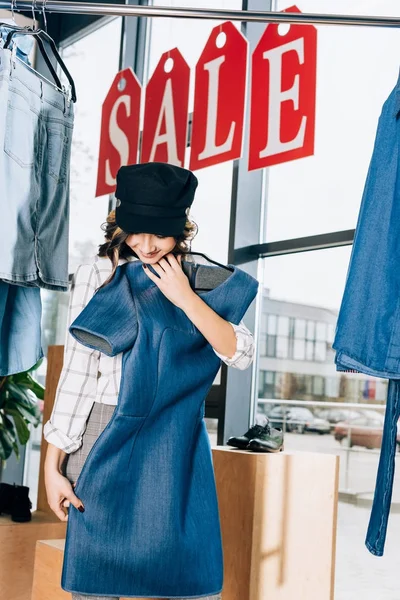 Mujer joven feliz mirando el vestido de mezclilla azul en la tienda de ropa - foto de stock