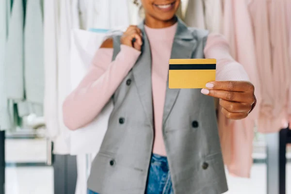 Hermosa joven mostrando tarjeta de crédito en la tienda de ropa - foto de stock
