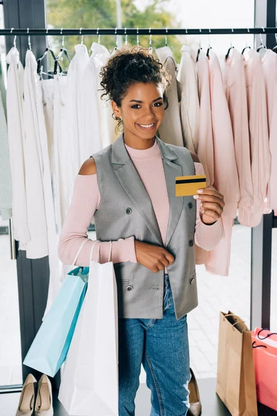 Hermosa joven mostrando tarjeta de crédito en la tienda de ropa - foto de stock