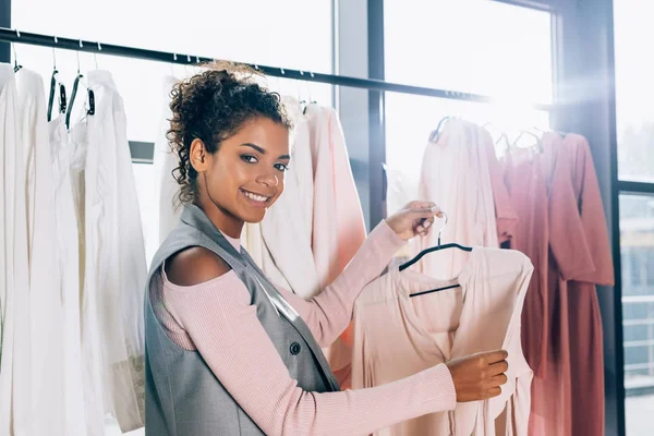 Happy beautiful shopper looking for new clothes on hangers in store — Stock Photo