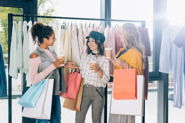 Groupe de jeunes femmes avec sacs à provisions et café pour aller dans le magasin de vêtements — Photo de stock