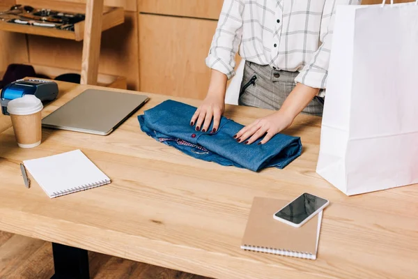 Colpo ritagliato della camicia pieghevole del direttore del negozio di abbigliamento per imballarla nella borsa della spesa — Foto stock