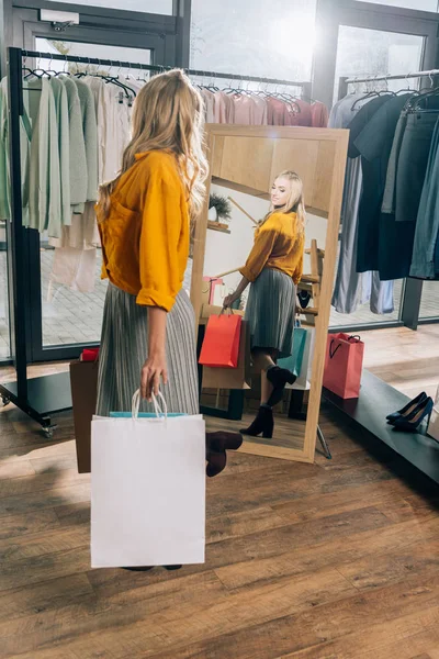 Bella giovane donna guardando specchio nel negozio di abbigliamento — Foto stock