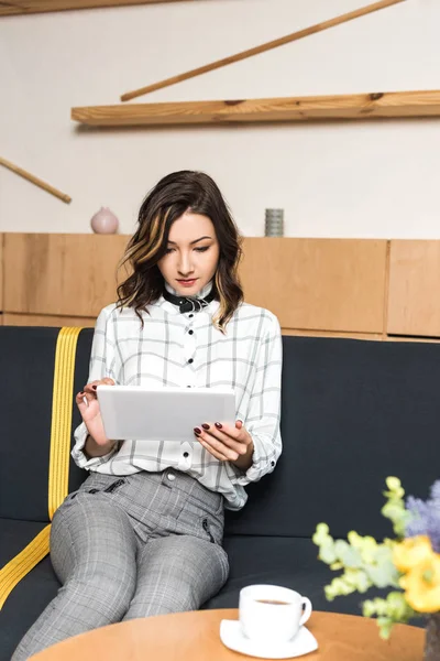 Молода жінка використовує планшет, сидячи на дивані в кафе — стокове фото