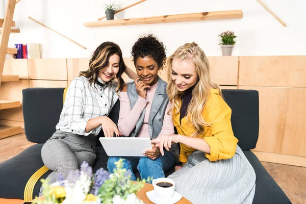 Group of happy girlfriends using tablet together in cafe — Stock Photo