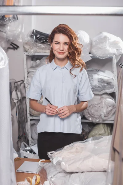 Beautiful young female dry cleaning worker at warehouse with many plastic bags — Stock Photo