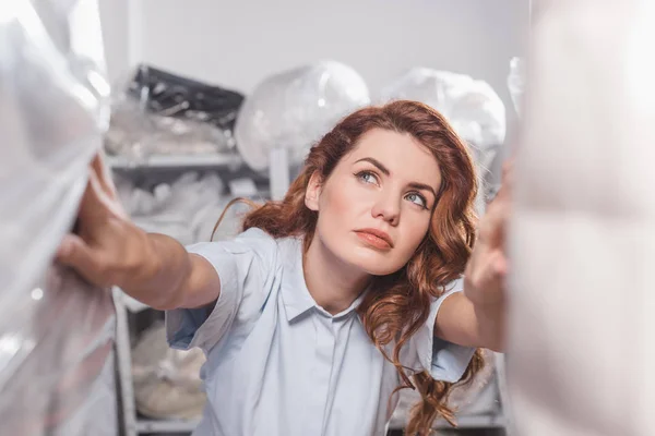 Female dry cleaning worker looking at clothing packed in plastic bags — Stock Photo