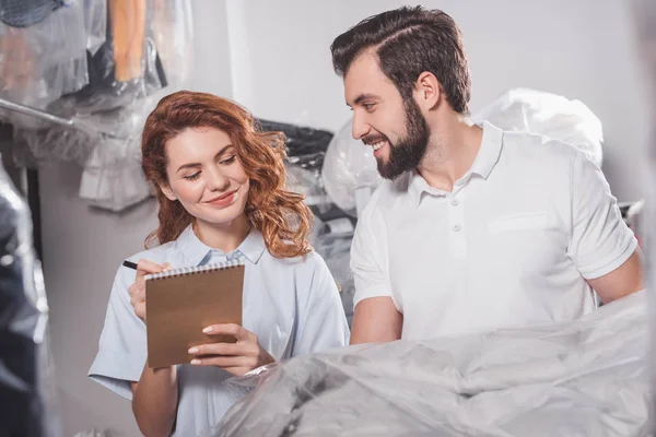 Young dry cleaning workers with jacket in bag at warehouse — Stock Photo