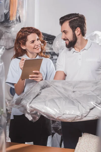 Happy dry cleaning workers with jacket in bag at warehouse — Stock Photo