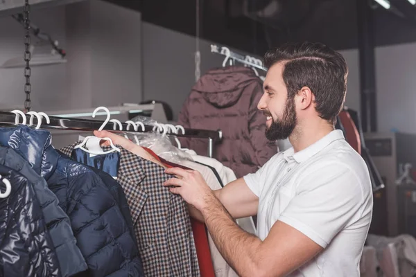 Handsome young dry cleaning worker hanging jacket at warehouse — Stock Photo