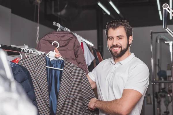 Happy young dry cleaning worker hanging jacket at warehouse — Stock Photo