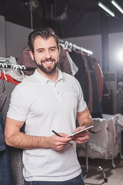 Happy dry cleaning worker with notepad at warehouse — Stock Photo