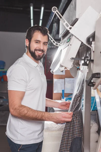 Happy young dry cleaning worker packing jacket in plastic bag — Stock Photo