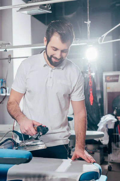 Dry cleaning worker using industrial iron at warehouse — Stock Photo