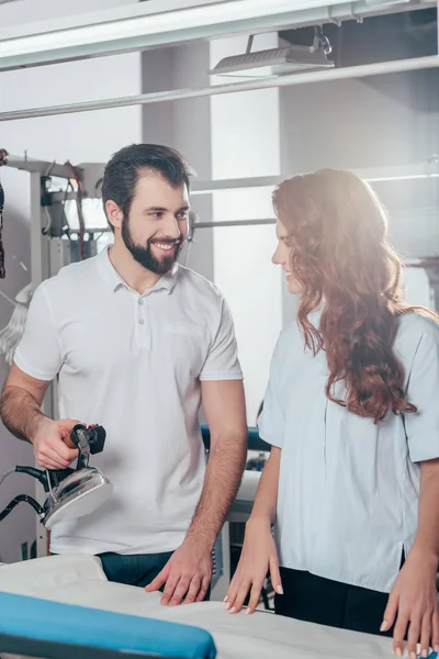 Sonrientes jóvenes trabajadores de limpieza en seco planchando ropa - foto de stock