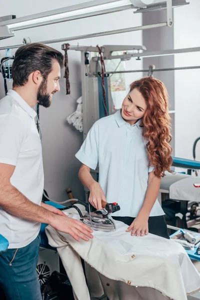 Happy young dry cleaning workers ironing clothes — Stock Photo