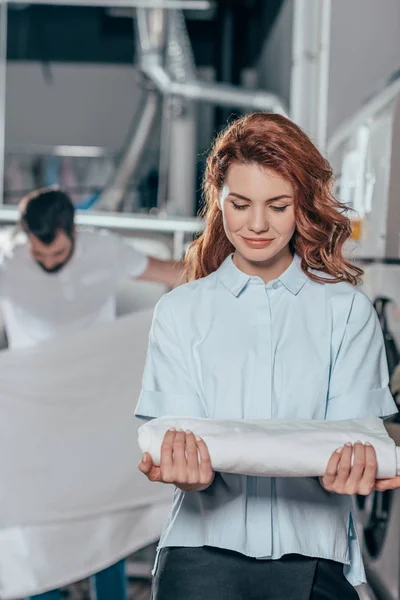 Attractive young dry cleaning manageress holding clean clothes — Stock Photo