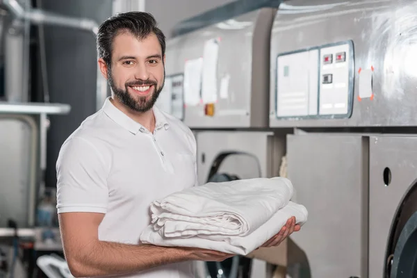 Trabalhador de limpeza a seco feliz segurando pilha de roupas limpas — Fotografia de Stock