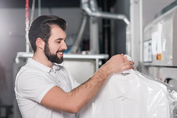 Trabalhador de limpeza a seco segurando sacos com roupas limpas — Fotografia de Stock