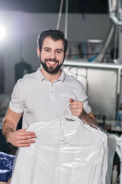 Trabalhador de limpeza a seco com camisa limpa no cabide em saco plástico — Fotografia de Stock