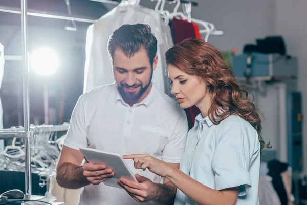 Felices jóvenes trabajadores de limpieza en seco utilizando tabletas juntos - foto de stock